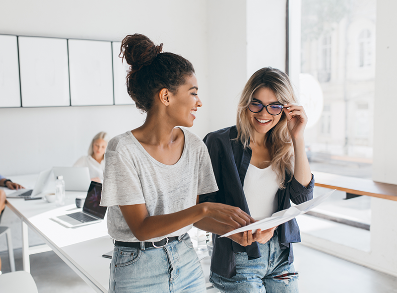 Zwei Frauen zeigen lächelnd auf ein Blatt Papier
