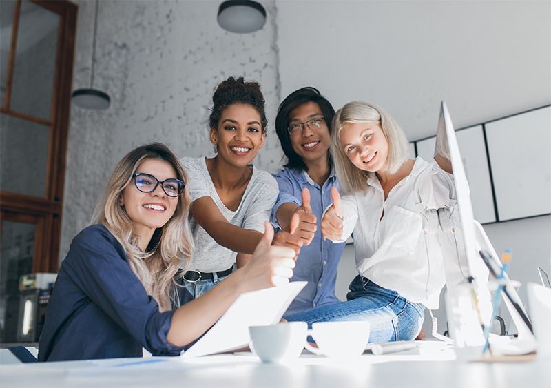 Lächelndes Team im Büro zeigt Daumen nach oben