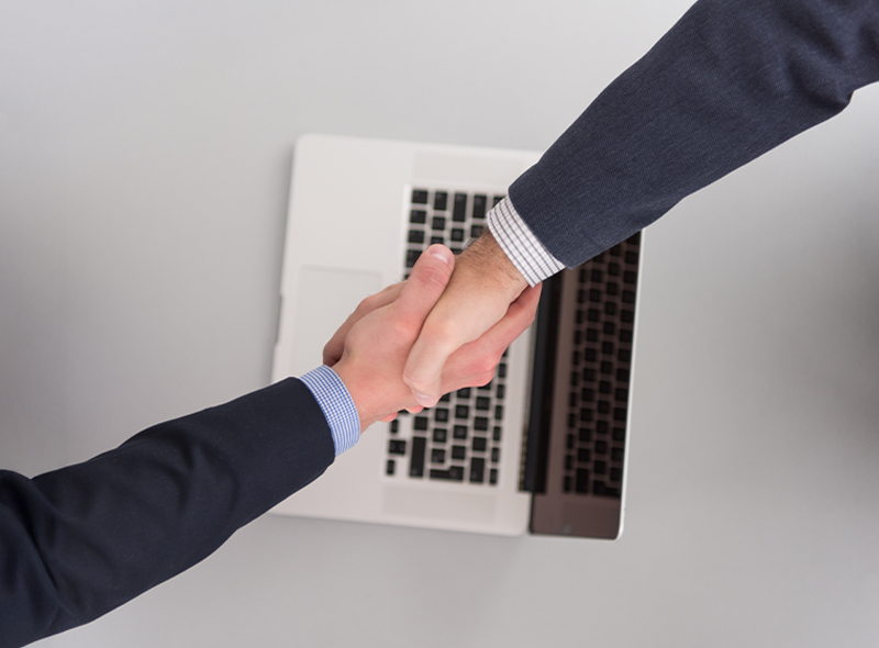 Partnerschaftlicher Handschlag über Laptop für etablierte IT-Lösungen